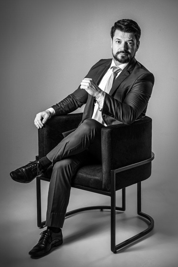 Retrato de homem com expressão séria, em fundo escuro, iluminação lateral destacando os traços faciais. Imagem forte e sofisticada.