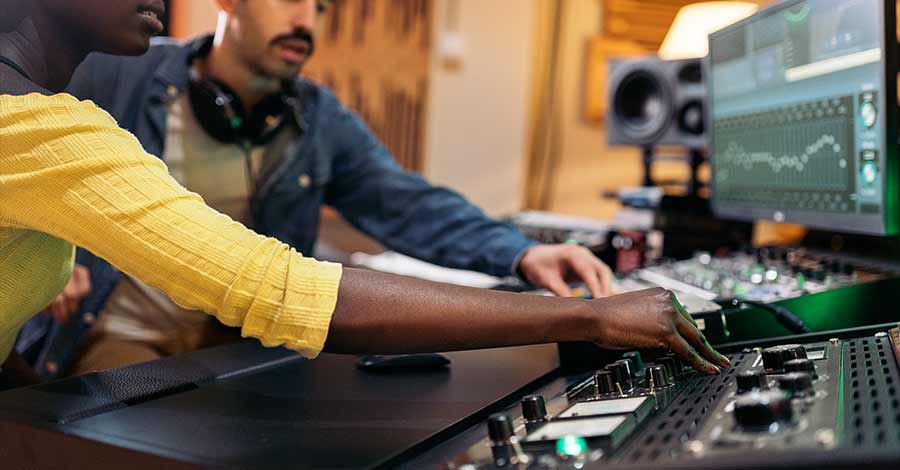 Pessoa trabalhando em uma estação de edição de vídeo profissional com painel de correção de cor, usando monitores grandes em um ambiente escuro.