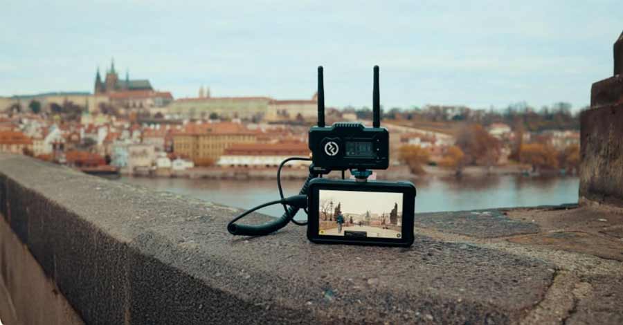 Dispositivo transmissor de vídeo Hollyland conectado a um monitor externo exibindo uma paisagem urbana com rio e arquitetura histórica ao fundo.
