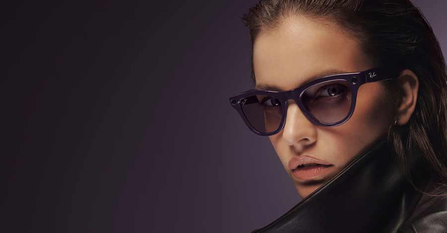 Mulher com expressão séria usando óculos escuros Ray-Ban em um fundo escuro.