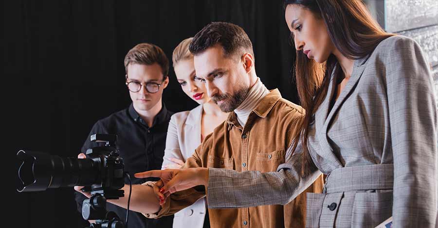 Grupo de quatro pessoas observa a tela de uma câmera fotográfica em um estúdio, discutindo o enquadramento.
