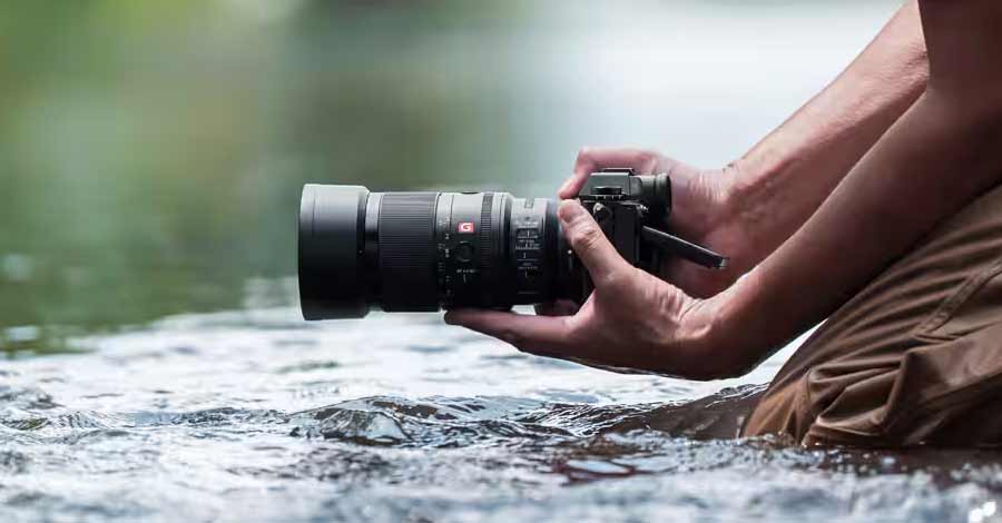 Fotógrafo segura câmera profissional próximo à água, capturando imagens em ambiente natural.