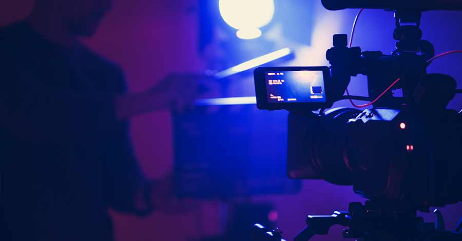 Câmera profissional filmando em estúdio com luz azul e operador preparando o cenário para gravação de vídeo.
