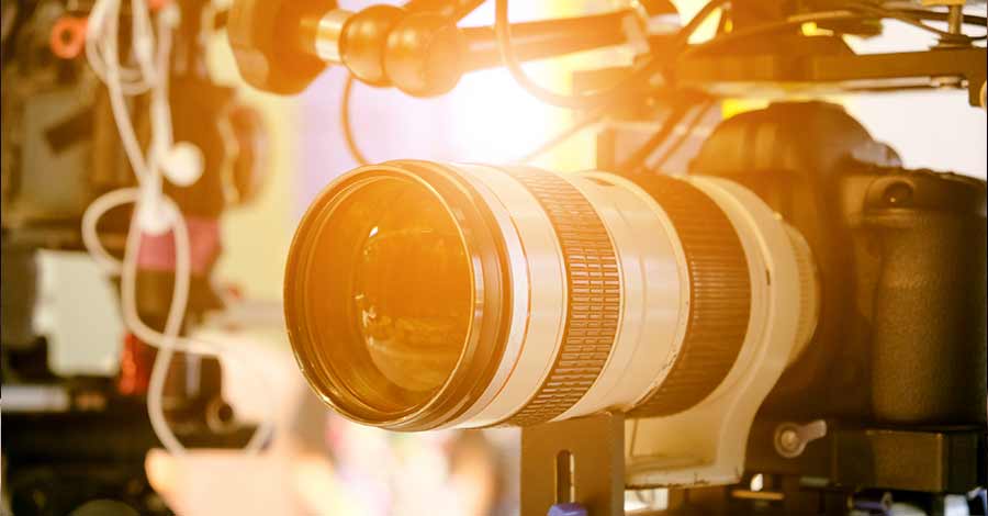 Câmera profissional equipada com lente teleobjetiva e acessórios de vídeo, iluminada por luz quente em ambiente de gravação.