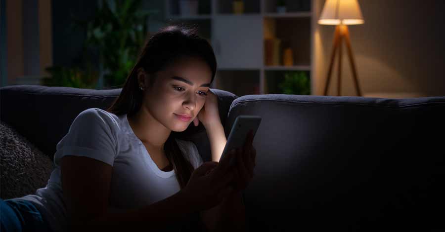 Mulher usando celular no escuro em ambiente doméstico iluminado por abajur